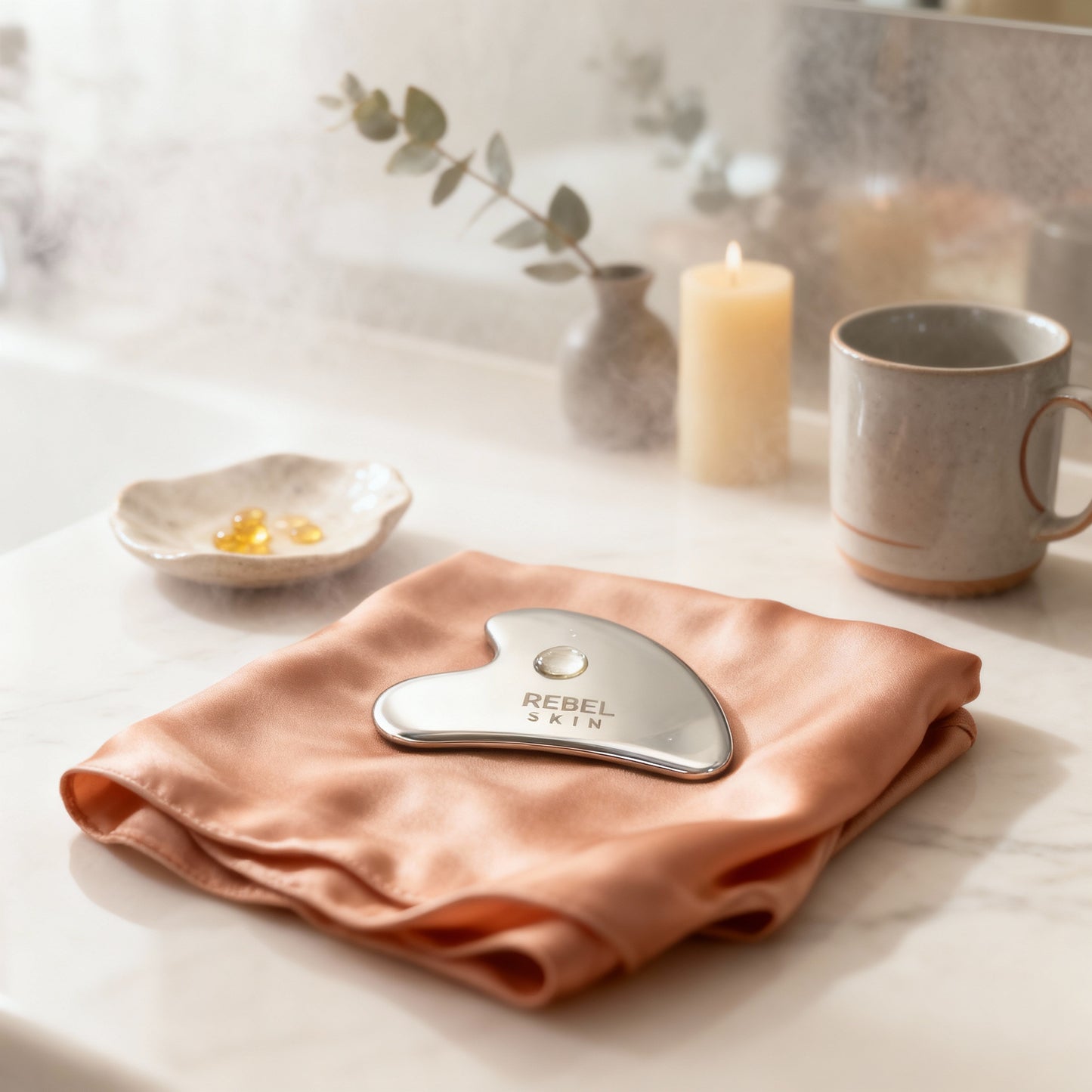 Gua Sha tool on a pink towel with a blurred background of a candle and mug.